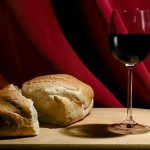 An image of a wine filled in a glass and piece of bread that placed on the table.