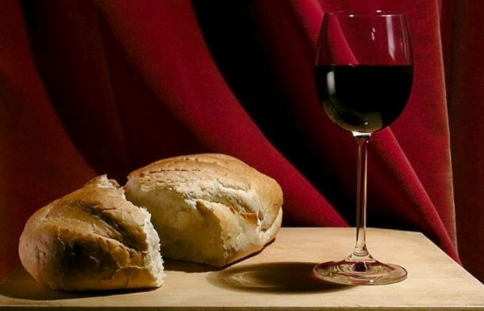 An image of a wine filled in a glass and piece of bread that placed on the table.